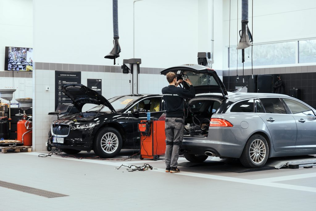 Mekaniker står bal en grå bil med bagasjeluken åpen på bilverksted