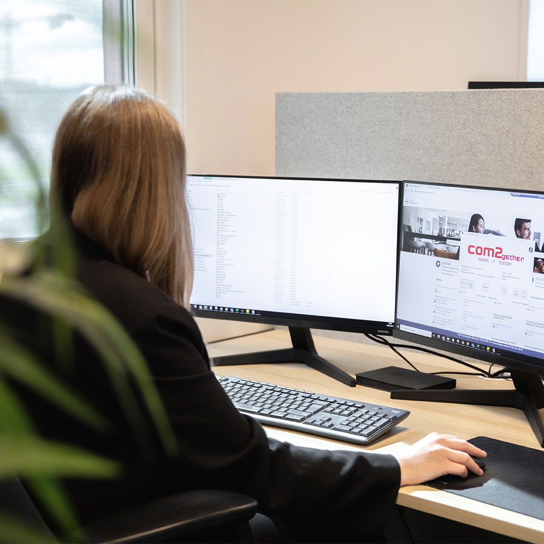 Kvinne sitter med ryggen til og jobber på to pc-skjermer