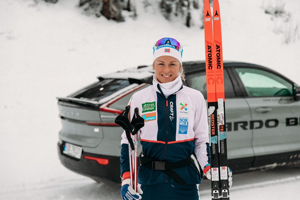 Kvinne (Anne KJersti Kalvå) holder et par langrennski foran en bil i vinterlandskap