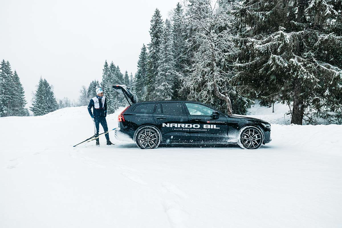 Mann står bak en svart Volvo med bagasjeluken åpen i vinterlandskap