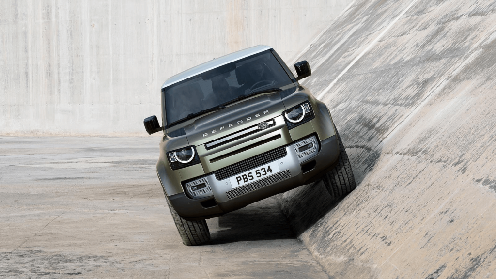 Grønn Land Rover parkert skrått med halve bilen stående i en bratt bakke
