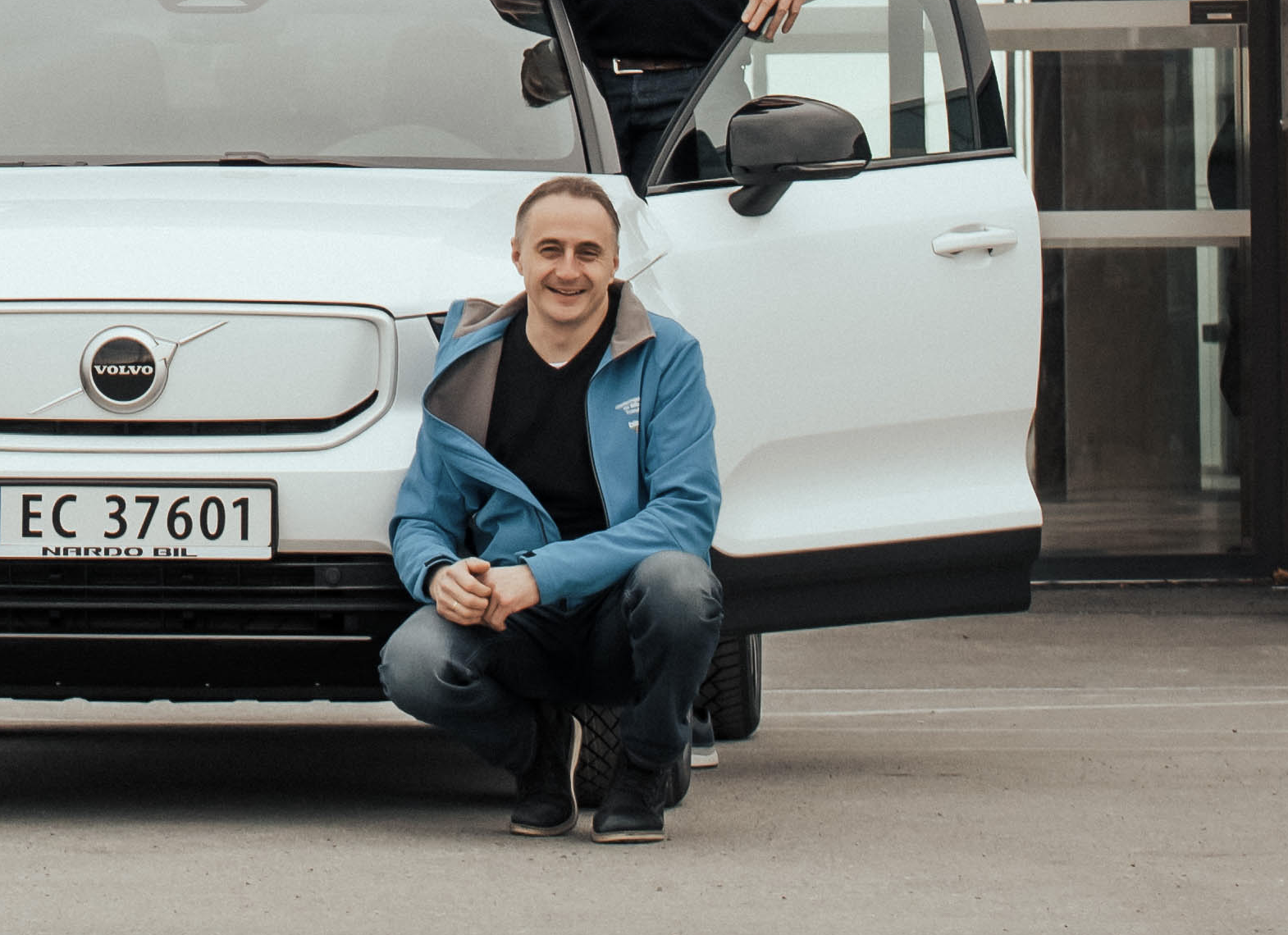 Mann sitter på huk foran hvit Volvo