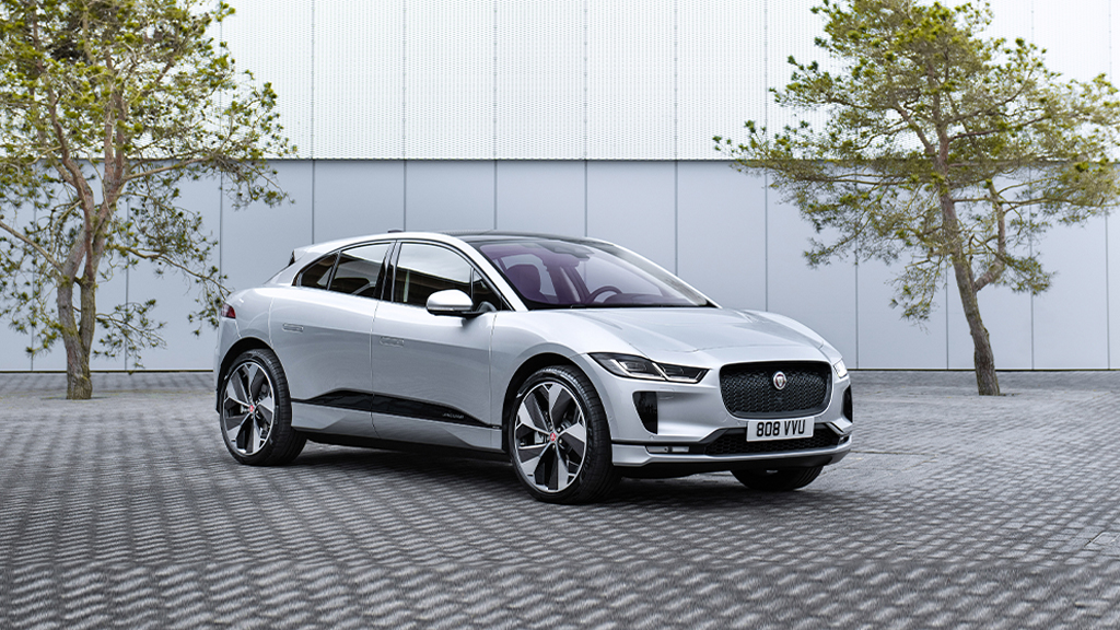 Sølvfarget Jaguar parkert på hellelagt underlag med to trær i bakgrunnen