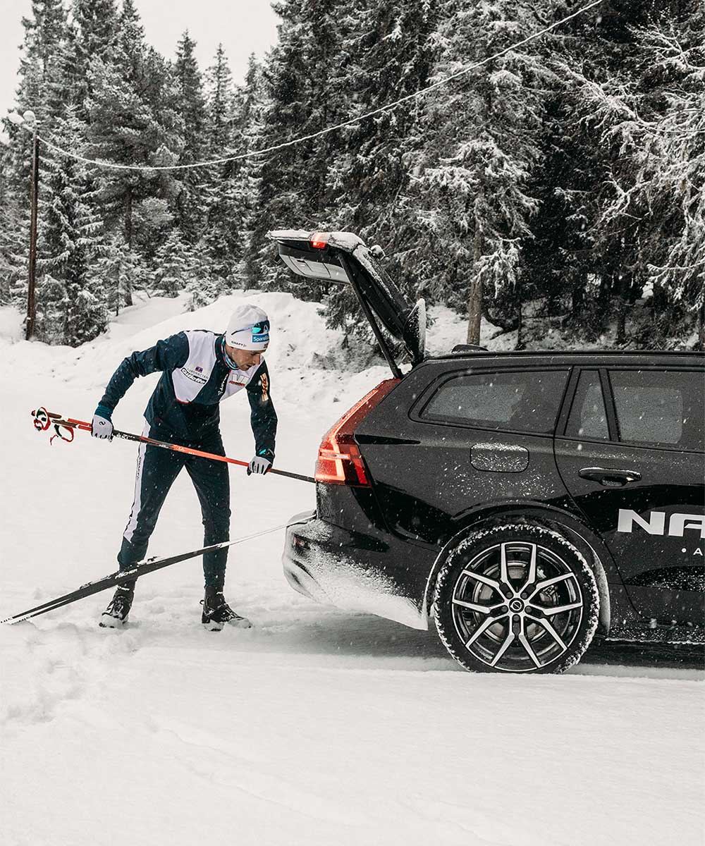 Mann legger et par skistaver inn i svart Volvo