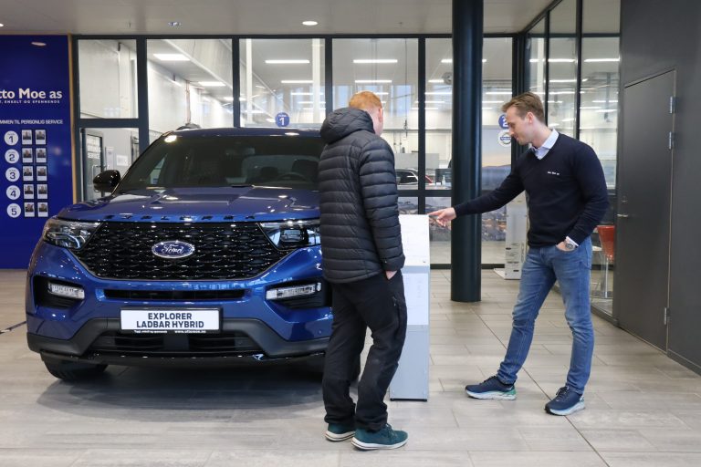 Bilselger og kunde ser på en blå Ford i en bilforretning